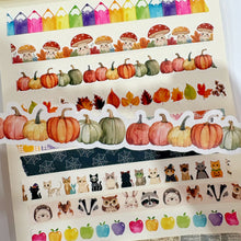 Lade das Bild in den Galerie-Viewer, A collection of decorative washi tapes with autumn and animal motifs, displayed on a cream-colored notebook page. The tapes feature watercolor pumpkins, colorful pencils, mushrooms, autumn leaves, cats, dogs, owls, raccoons, hedgehogs, and vintage script text.