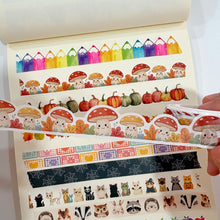 Lade das Bild in den Galerie-Viewer, A hand holds a roll of washi tape featuring cute cartoon mushrooms, pumpkins, and autumn leaves over an open notebook filled with other colorful patterned washi tapes.